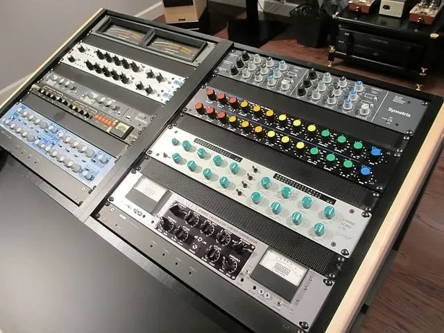 Professional audio mixing console with various knobs, sliders, and meters in a studio setting by Sage Audio.