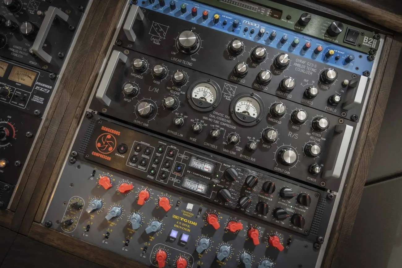 Close-up of professional audio mixing, mastering, and recording equipment with various knobs, meters, and switches.