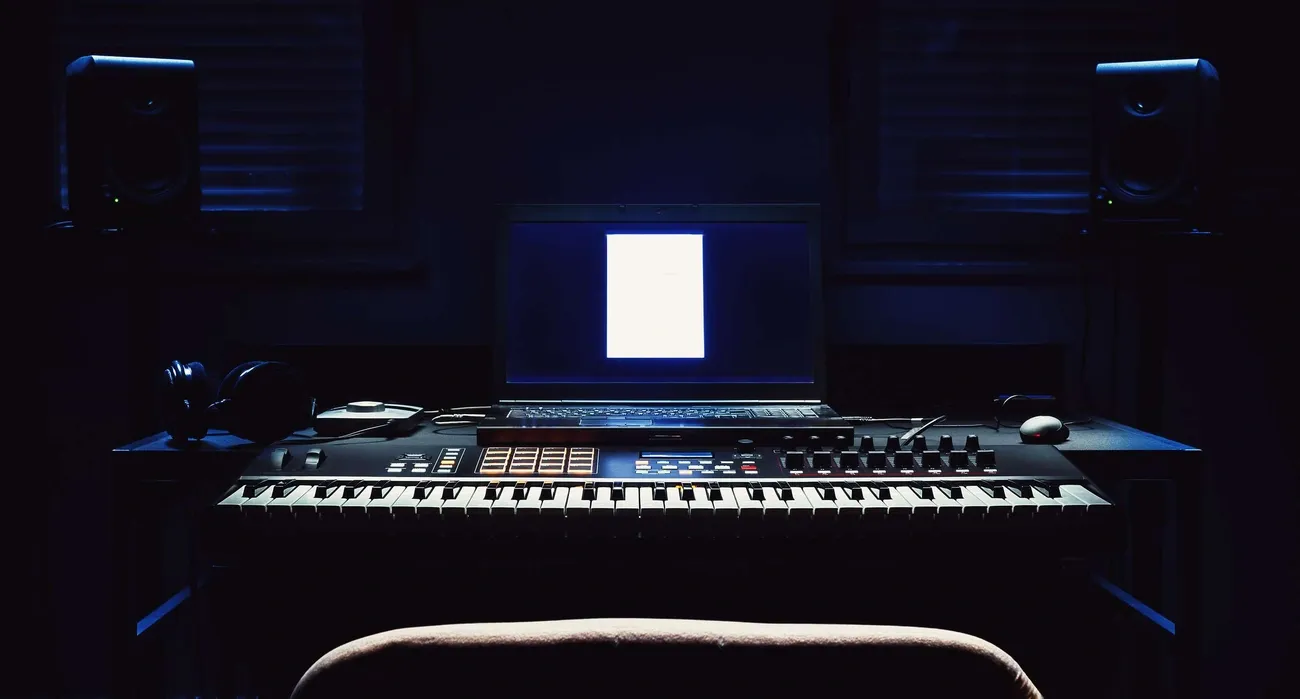 Dimly lit music studio setup with keyboard, laptop, headphones, and speakers for mastering music.