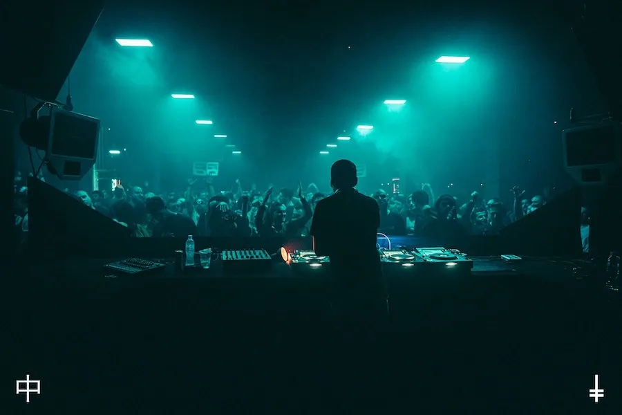 DJ performing at a packed Berlin techno party with blue-green lighting and an energetic crowd in May 2024.