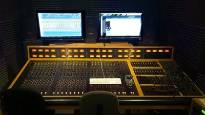 Professional audio studio control room with analog mixing console and dual screens, showcasing mastering eq settings.