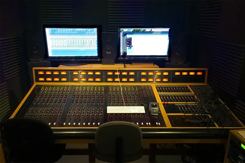 Professional audio studio control room with analog mixing console and dual screens, showcasing mastering eq settings.