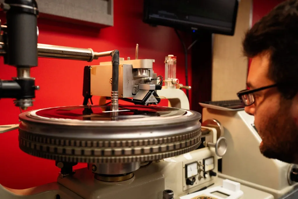 Close-up of a vinyl mastering machine engraving a record in a studio with red walls.