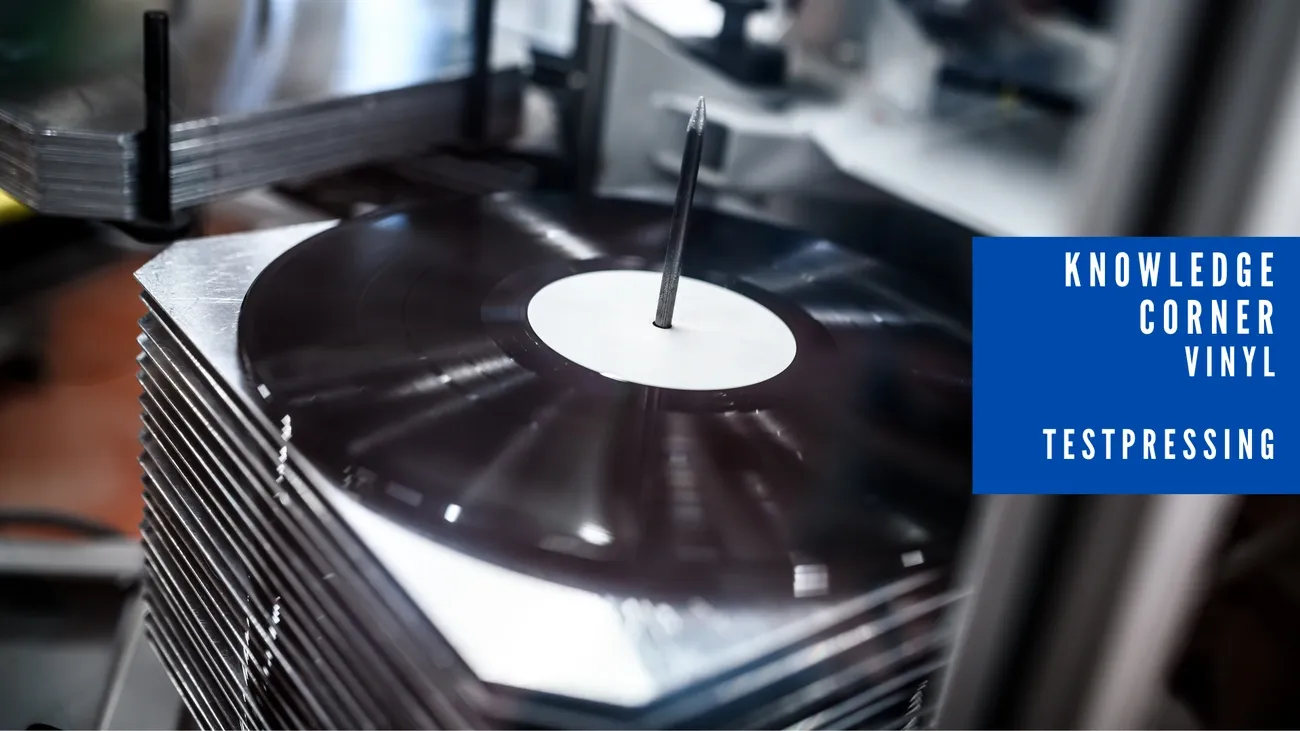 Stack of vinyl test pressings being processed on a spindle in a pressing facility.